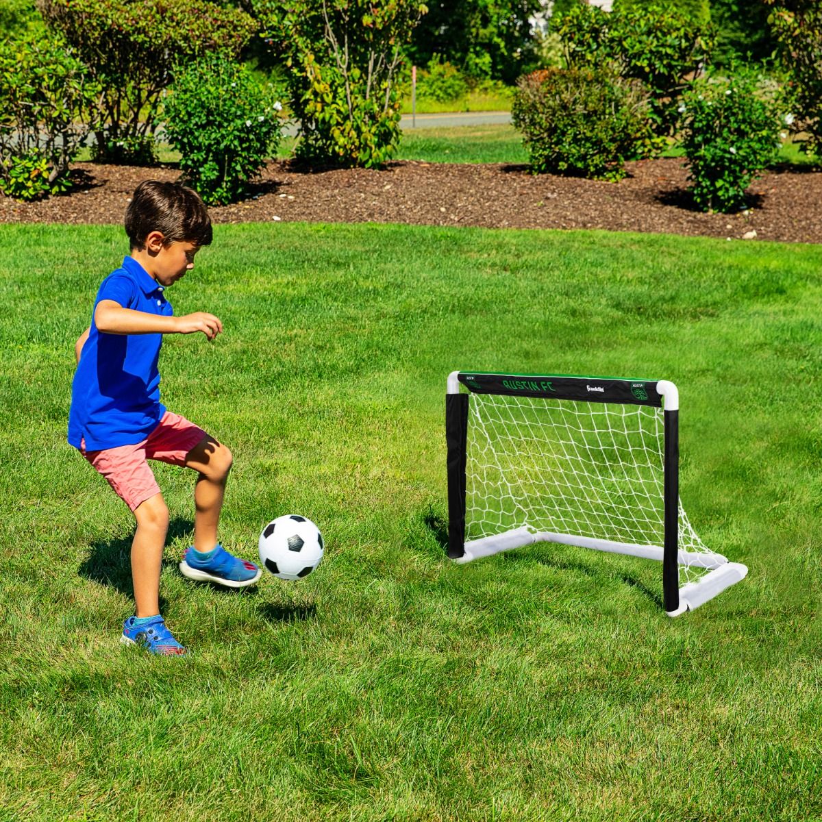 Child playing soccer with a goal on a grassy field