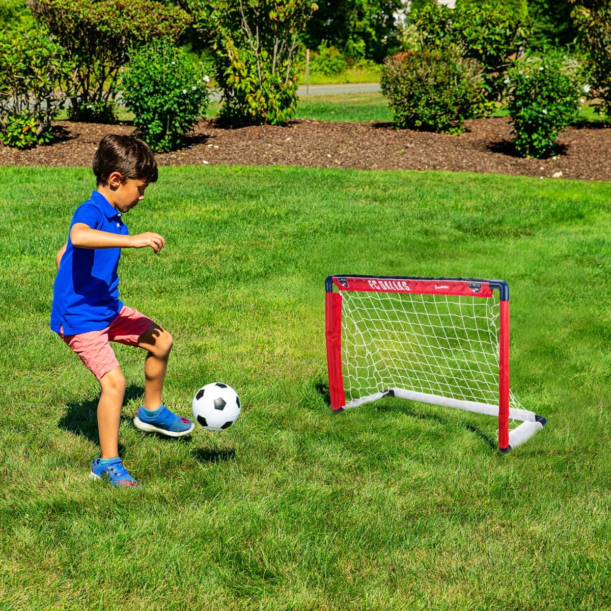 Child playing soccer with a goal and ball on a grassy field