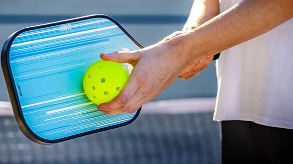 Person holding a pickleball paddle and ball on a court